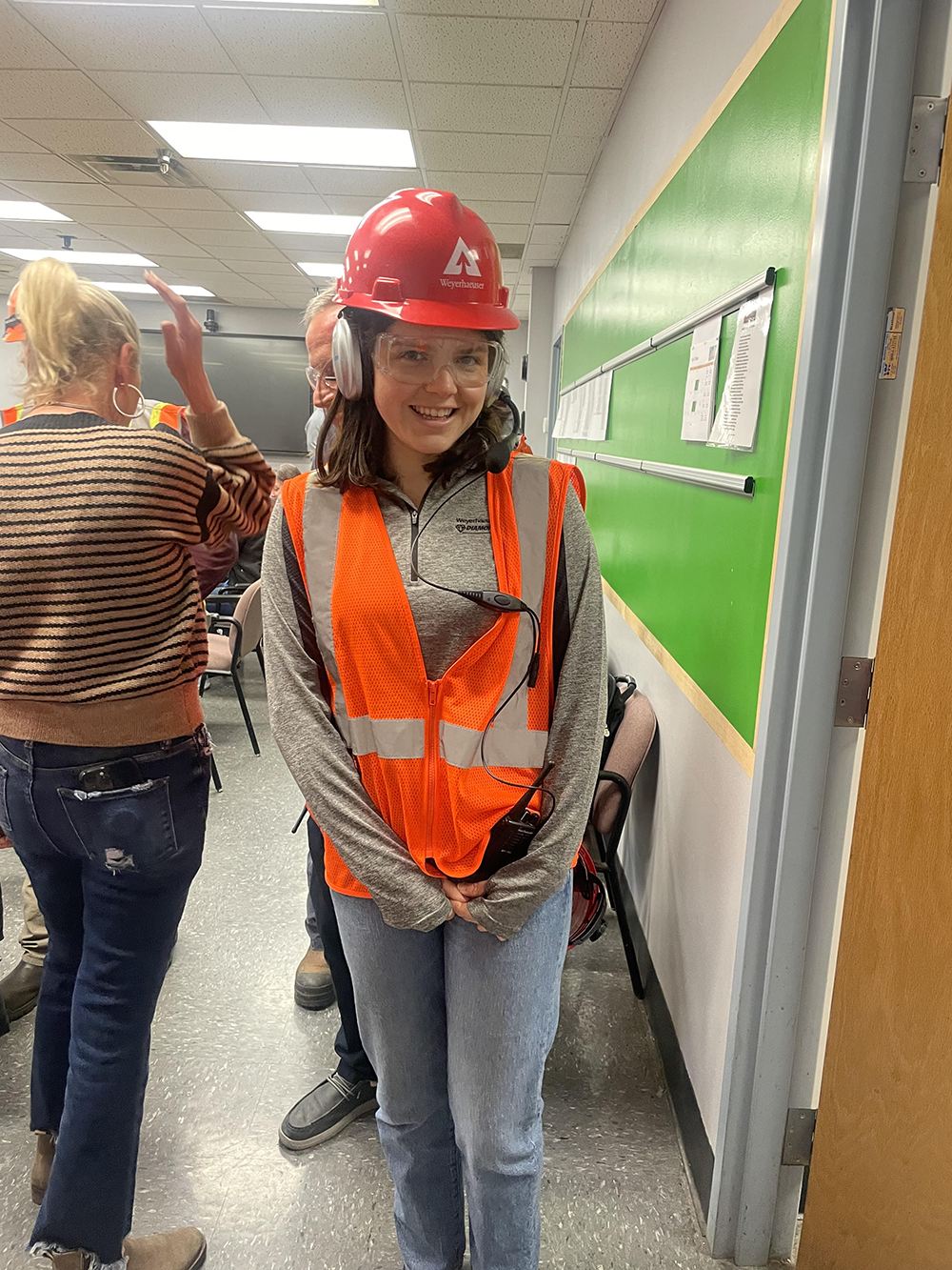Image of Ashley wearing a red Weyerhaeuser hard hat and orange safety vest while visiting West Virginia's OSB mill on her first week of work. 